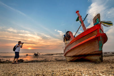 Man photographing boat at beach during sunset