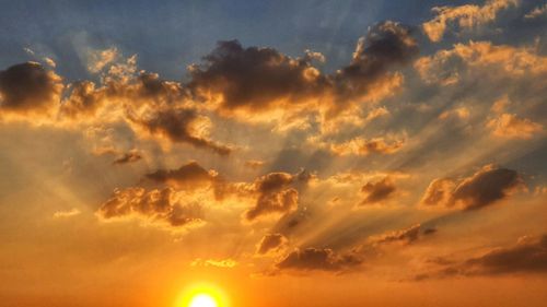 Low angle view of sunlight streaming through clouds during sunset