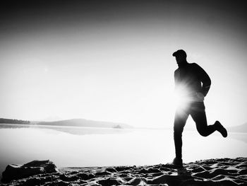 Silhouette man standing by lake against clear sky