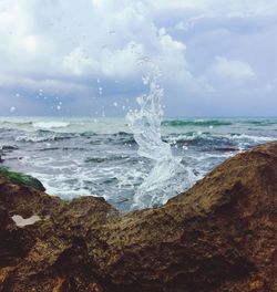 Waves splashing on rocks at shore against sky