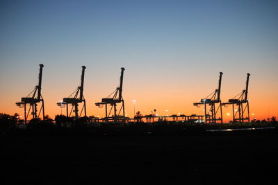 Silhouette of cranes at harbor against sky during sunset