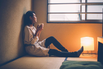 Side view of young woman using mobile phone at home