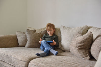 Boy sitting on sofa at home and playing tablet