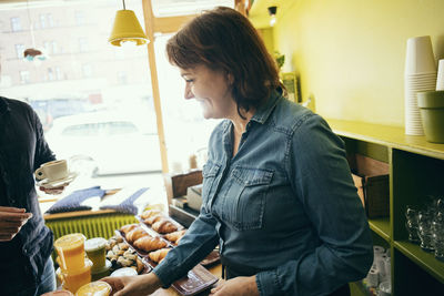 Smiling female owner serving drinks to customer in coffee shop