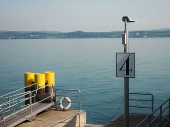 Arrow sign by sea against sky