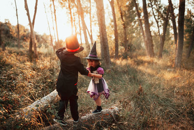 Girl wearing witch hat standing with brother at forest during halloween