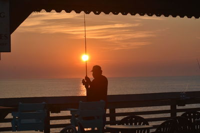 Silhouette man sitting by sea against sky during sunset