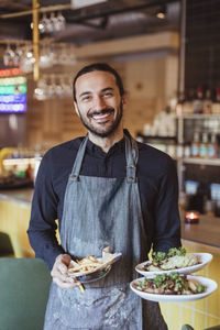 Portrait of smiling male waiter with food in restaurant