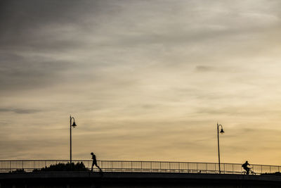 Silhouette people standing on bridge against sky during sunset