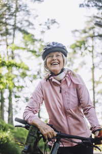 Smiling senior woman looking away while standing with cycle