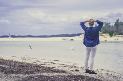 Rear view of woman with head in hands standing on shore at beach