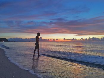 Man standing on beach against sky during sunset