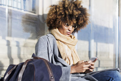 Woman using mobile phone while sitting at bus stop