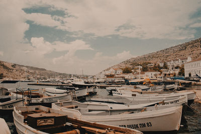 Boats moored at harbor against cloudy sky