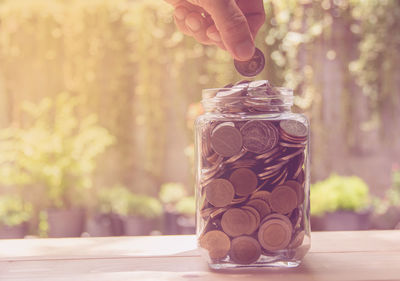 Cropped hand of man putting coins in jar on table