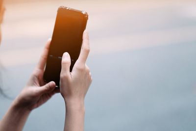 Midsection of woman holding smart phone against sky