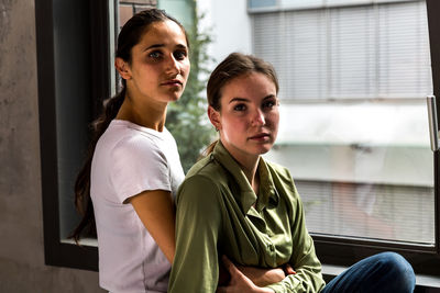 Portrait of lesbian couple against window at home