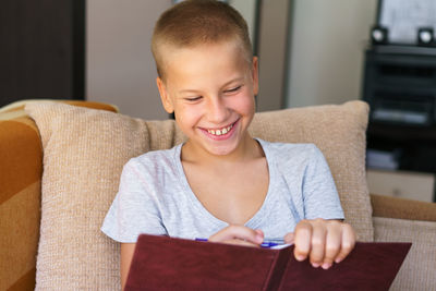 Portrait of schoolboy sitting on sofa doing homework, happy child, boy holding