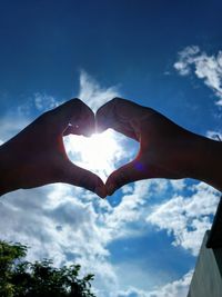 Low angle view of hand holding heart shape against sky