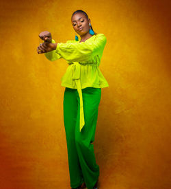 Young woman looking away while standing against yellow background