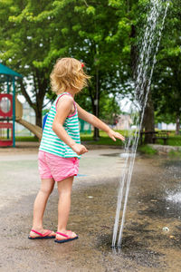 Little happy kid playing with water at splash pad fountain in local public park on hot summer day. 