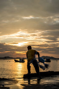 Fisherman throwing net at jetty during sunset