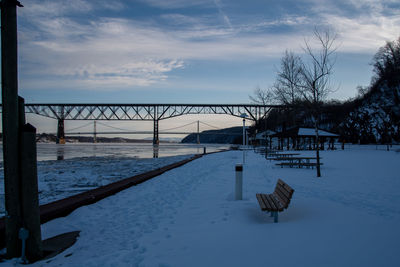 Empty benches on snow covered bench against sky during winter