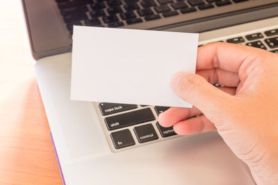 Close-up of woman holding blank paper by laptop on table