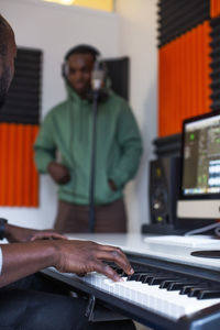 Hands of sound engineer playing piano while rapper standing in recording studio