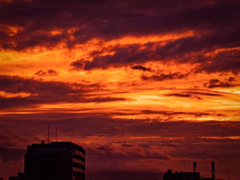 Low angle view of silhouette buildings against dramatic sky during sunset