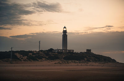 Lighthouse by sea against sky during sunset