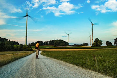 Man standing on field by road against sky