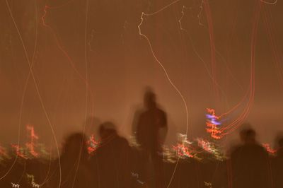 Light trails and people at night against sky