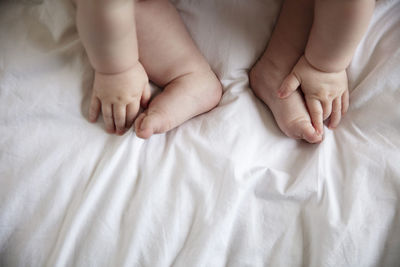 Low section of baby hands touching feet on bed