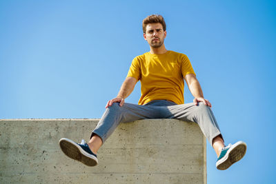 Portrait of young man sitting against clear blue sky