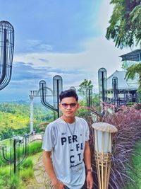 Portrait of young man standing by plants against sky