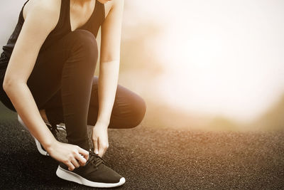 Low section of woman tying shoelace while crouching outdoors