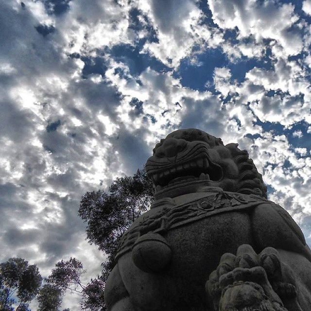 sky, low angle view, cloud - sky, cloud, statue, tree, sculpture, cloudy, human representation, nature, tranquility, art, art and craft, day, beauty in nature, rock - object, outdoors, no people, creativity