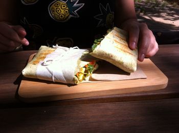 Midsection of person holding wrap sandwich on serving board