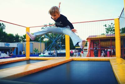 Full length of girl jumping on trampoline at amusement park against clear sky