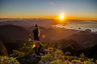 Woman standing on rock against sky during sunset