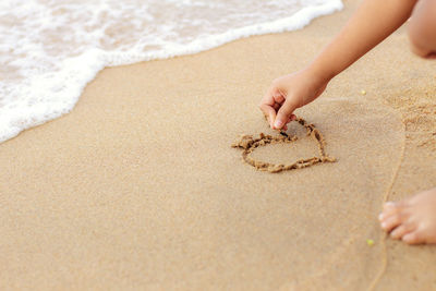 Low section of girl playing on sand at beach