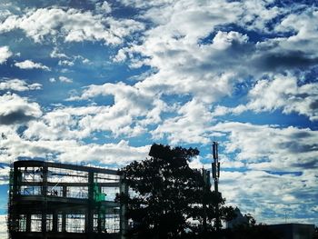 Low angle view of silhouette trees by building against sky