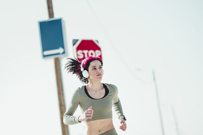 Woman with headphones looking away while running against sign board