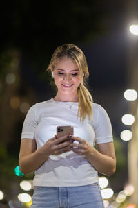 Woman using a smartphone at night time on the street. mobile phone, technology, urban .