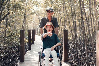 Father with disabled boy on wheelchair against trees