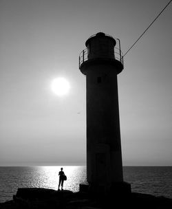 Lighthouse on beach against sky at sunset