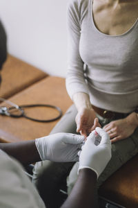 Doctor wearing gloves checking blood sugar level of female patient in clinic