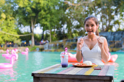 Portrait of woman eating food against swimming pool
