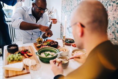 Mature friends with shaved head having food while sitting at table